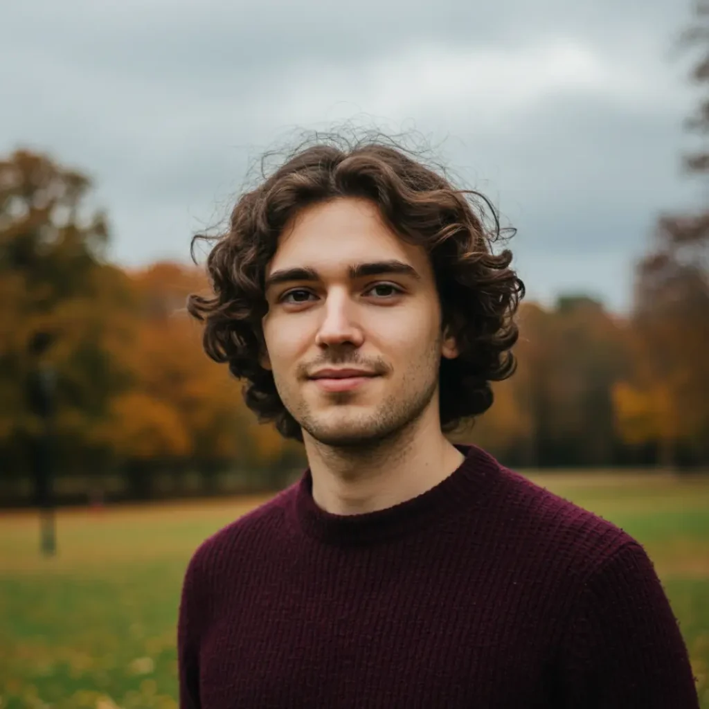 Henry Kane with curly hair in a striped pastel shirt, standing in front of a colorful studio background